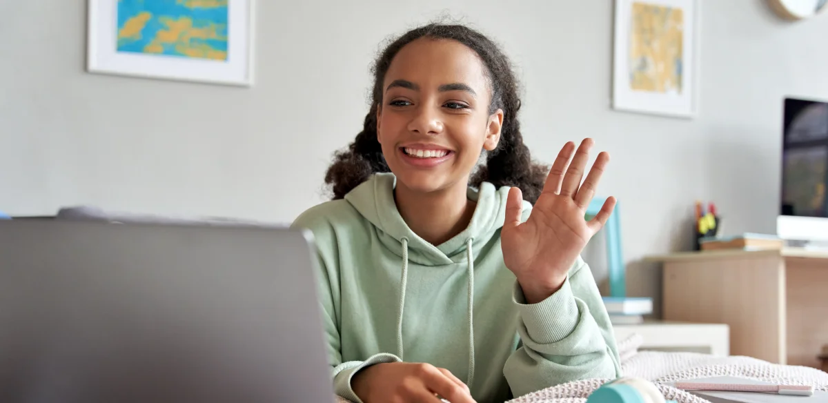 High school student waiving at her online class wearing a ligh green hoodie